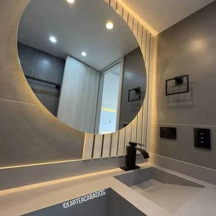 Baño con espejo redondo retroiluminado, lavamanos tallado y grifería negra